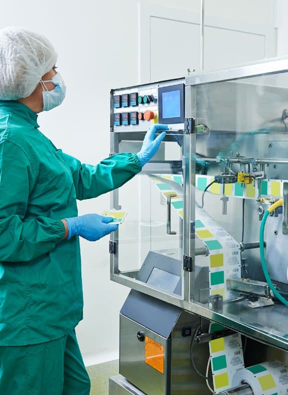 Machine operator monitoring packaging equipment in a controlled production area.